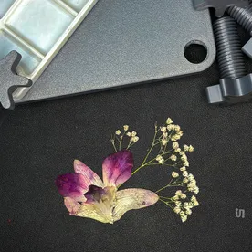 The Flower Keeper press beside a pressed orchid keepsake.
